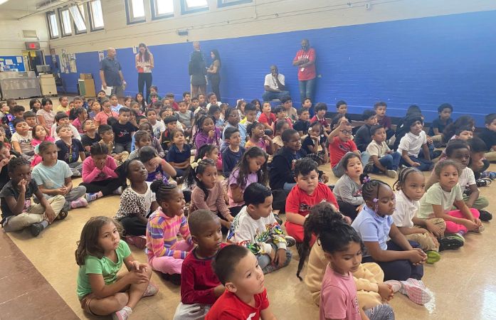 Students sitting on the floor with some staff members standing in the back. 